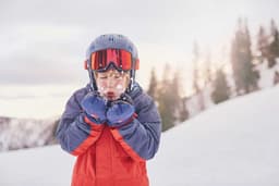 Kind im Skigewand pustet Schnee aus den Händen